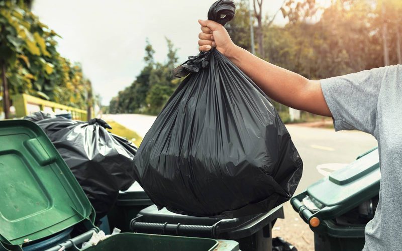 Person engaging in junk removal by disposing of a black garbage bag into trash bins outdoors on Cape Cod.