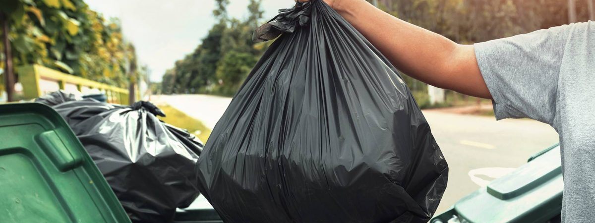 Person engaging in junk removal by disposing of a black garbage bag into trash bins outdoors on Cape Cod.