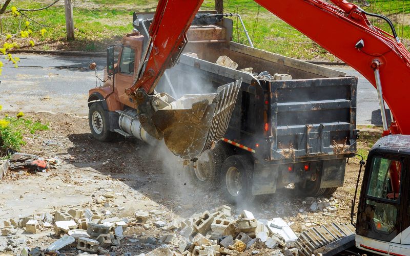 Excavator dumping debris into a truck for waste management at a construction site.