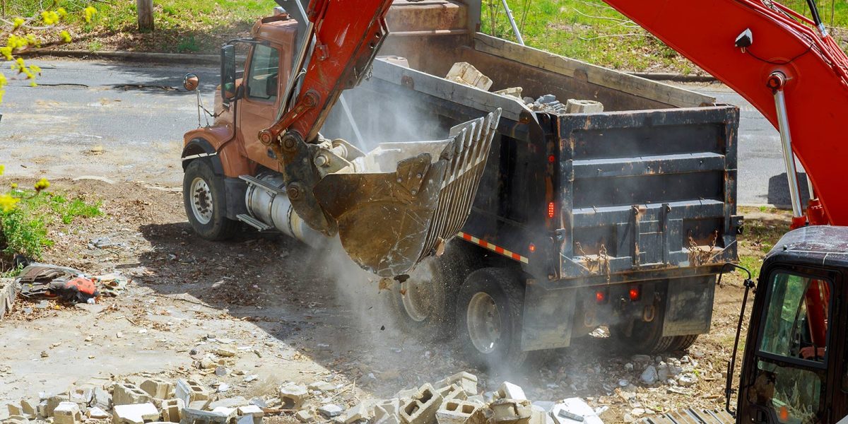 Excavator dumping debris into a truck for waste management at a construction site.