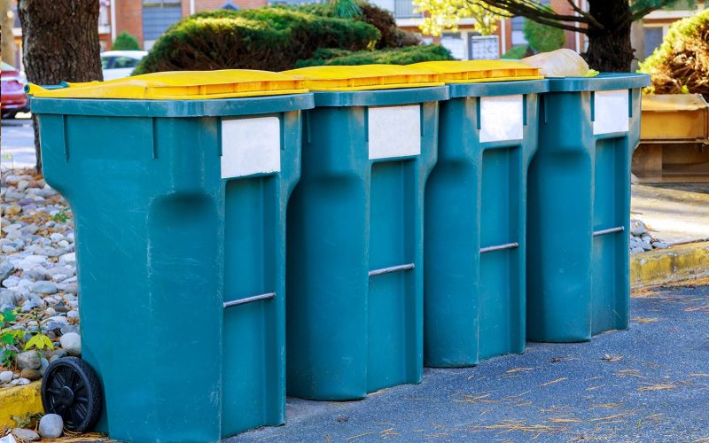 Row of blue recycling bins with yellow lids lined up on a Cape Cod street for disposal service.