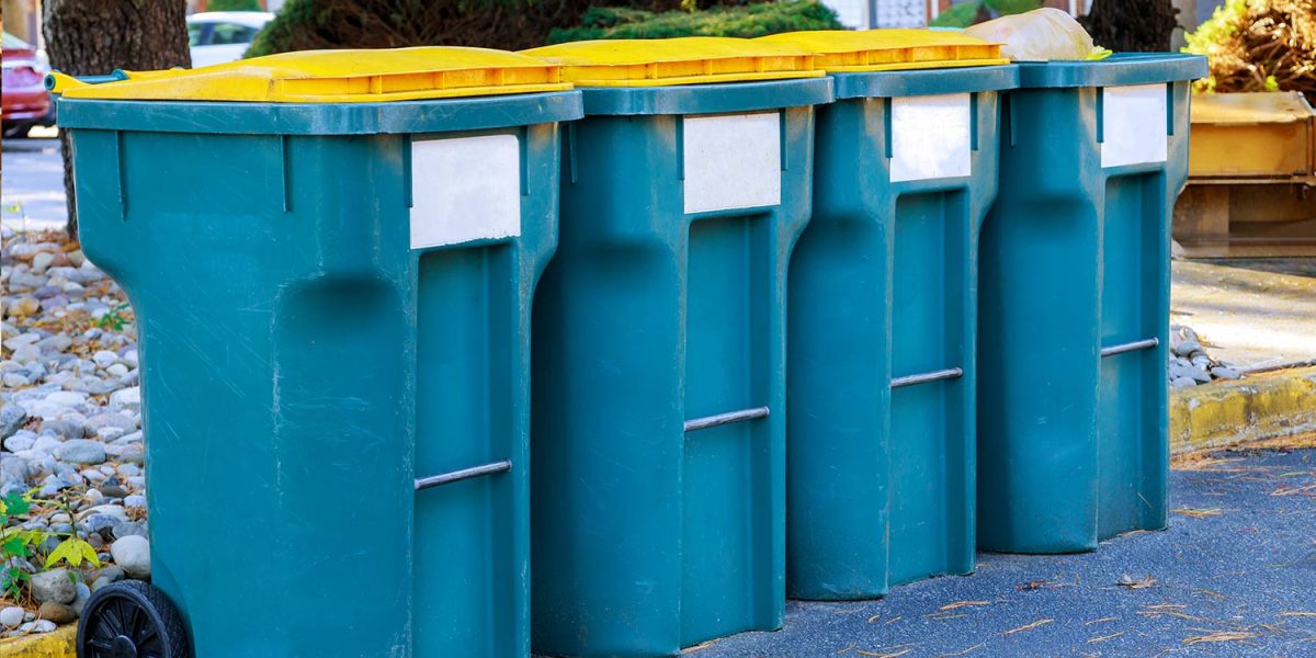 Row of blue recycling bins with yellow lids lined up on a Cape Cod street for disposal service.