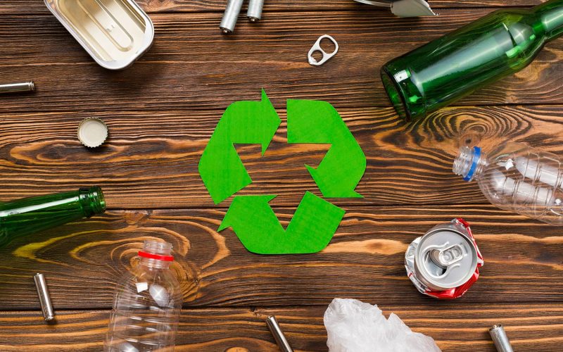 Recycling symbol surrounded by various types of waste on a wooden background, illustrating junk removal.