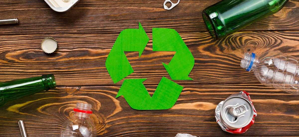 Recycling symbol surrounded by various types of waste on a wooden background, illustrating junk removal.